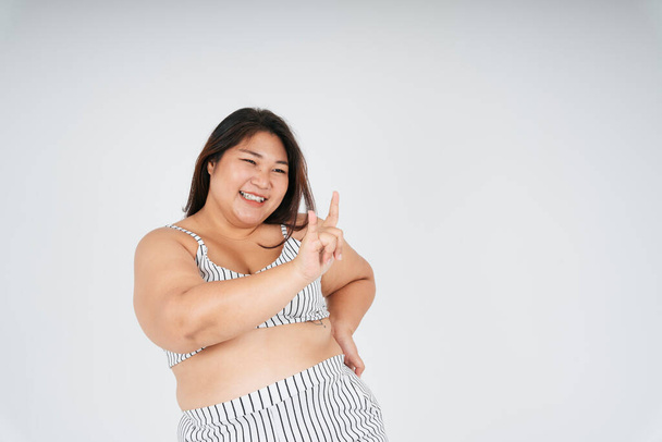 Portrait of asian fat woman in white sport bra with I love you gesture isolate over white background. - Photo, Image