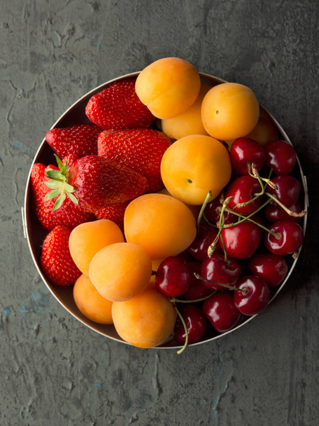 Baies fraîches mûres abricots, cerises et fraises dans un bol en fer. Vue du dessus,   - Photo, image