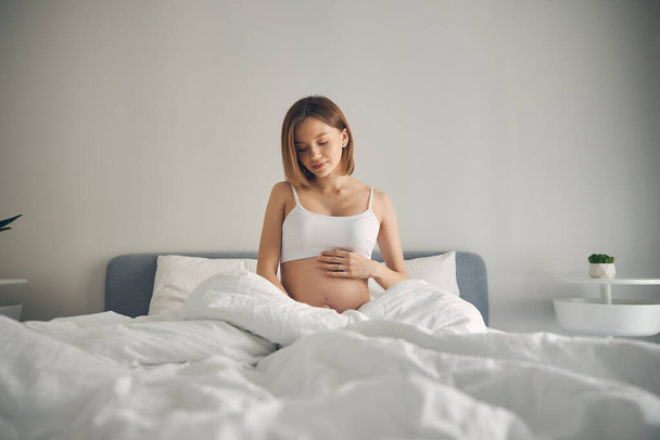 Attractive pregnant woman sitting in white bed - Photo, image