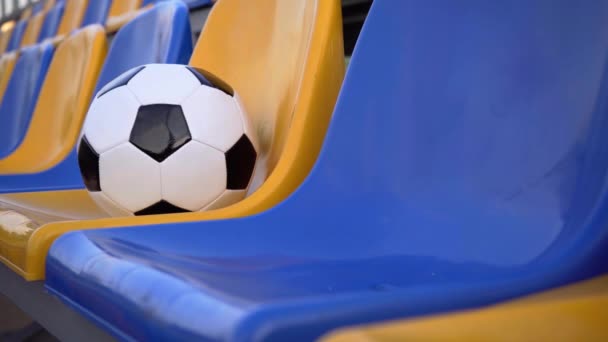 Zwarte en witte voetbal bal op een plastic stoel. Lege rijen en stoelen van een voetbalstadion. Leeg stadion tijdens quarantaine - Video