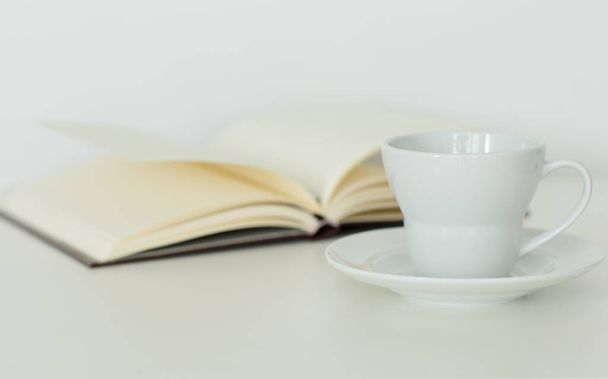 Carnet ouvert avec des pages blanches à plat à côté d'une tasse de café sur une soucoupe. Isolé sur fond blanc. Calme étude et détente. - Photo, image