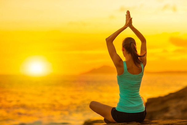 Gesundheit und Fitness - Junge gesunde, fitte Frau meditiert und praktiziert Yoga sitzend am Strand und beobachtet den schönen Sonnenuntergang über dem Meer. - Foto, Bild