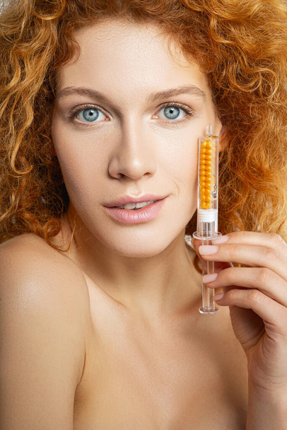 Beautiful young woman holding syringe with gold serum - Fotó, kép