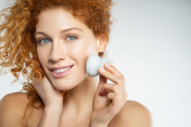 Beautiful young woman using facial cleaning massage brush - Fotoğraf, Görsel