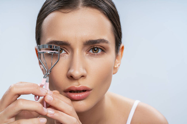 Beautiful young woman with perfect skin using eyelash curler - Photo, Image