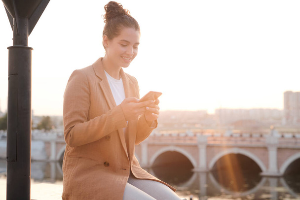 Inhalt Schöne junge Geschäftsfrau sitzt draußen und checkt Telefonnachricht, während sie online kommuniziert - Foto, Bild