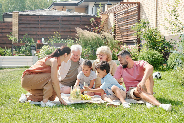 Große Mehrgenerationenfamilie picknickt an warmen Sommertagen auf Rasen im Hinterhof - Foto, Bild