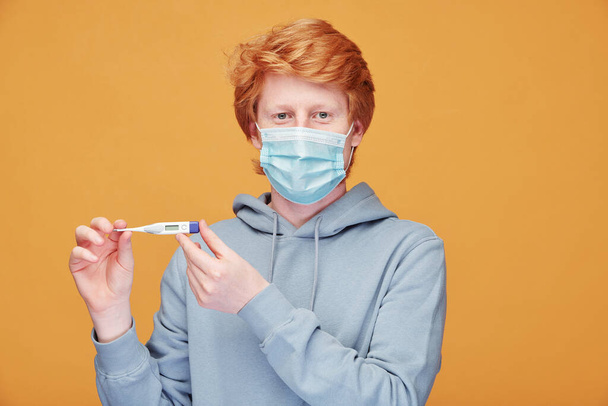 Portrait of smiling handsome young redhead man in hoodie applying toothpaste on toothbrush against orange background - Photo, image