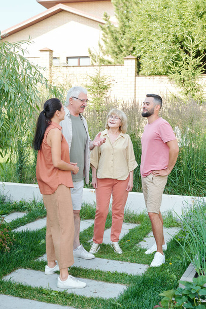 Gruppe von Senioren und jungen Erwachsenen, die an einem Sommertag zusammen im Hinterhof stehen und über etwas plaudern, Vollgas - Foto, Bild