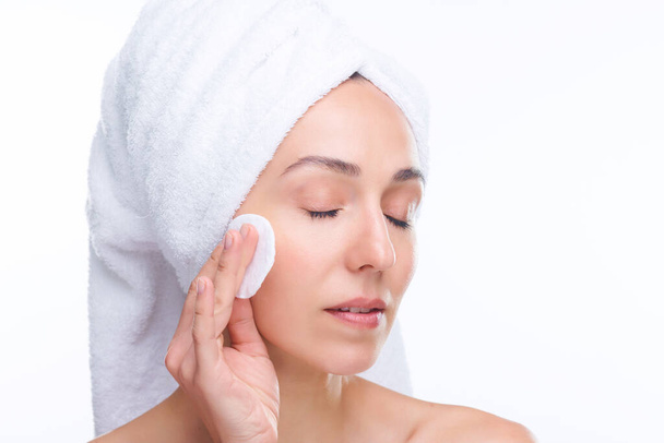 Młoda, piękna kobieta z podkładką z bawełny nakładającą płyn oczyszczający na twarz podczas pielęgnacji skóry po porannym lub wieczornym prysznicu - Zdjęcie, obraz