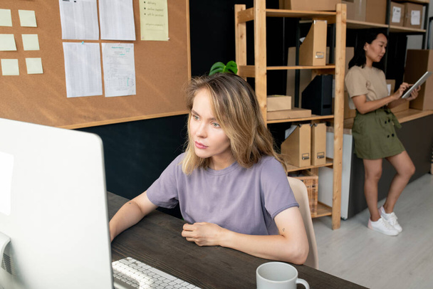 収納室の二人の現代的な若い女性労働者は、コンピュータとタッチパッドを使用して顧客のオンライン注文を確認し、取る。 - 写真・画像