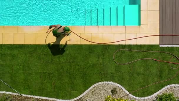 Luftaufnahme von männlichen Rasen Installateur Bewässerung neu platzierten Naturrasen und Reinigung Edge Fliesen von Freibad.  - Filmmaterial, Video