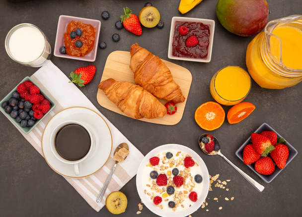 Frühstück serviert am Morgen mit Kaffee, Buttercroissant und Cornflakes Vollkorn und Rosinen mit Milch in Tassen und Erdbeere, Himbeere, Kiwi, frischer Orangensaft auf dem Frühstückstisch. - Foto, Bild