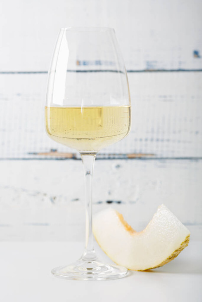 Glas witte wijn en een sneetje verse meloen op vintage houten tafel. Lichte achtergrond - Foto, afbeelding