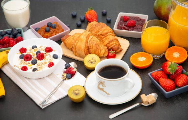 Ontbijt 's Ochtends geserveerd met koffie, botercroissant en cornflakes Hele granen en rozijnen met melk in kopjes en aardbeien, frambozen, Kiwi, verse sinaasappelsap op de ontbijttafel. - Foto, afbeelding