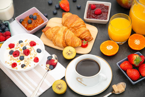 Desayuno servido por la mañana con café, croissant de mantequilla y copos de maíz Granos integrales y pasas con leche en tazas y fresa, frambuesa, kiwi, zumo de naranja fresco en la mesa de desayuno. - Foto, imagen