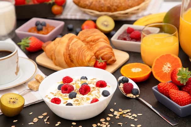 Desayuno servido por la mañana con café, croissant de mantequilla y copos de maíz Granos integrales y pasas con leche en tazas y fresa, frambuesa, kiwi, zumo de naranja fresco en la mesa de desayuno. - Foto, Imagen