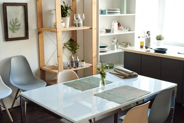 Белый прямоугольный пластиковый стол с кучей полевых цветов в вазе между двумя серыми салфетками в центре современной домашней комнаты или кухни - Фото, изображение