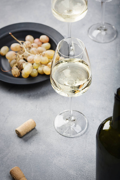Masanın üzerinde bir bardak beyaz şarap, üzüm ve bir şişe var. Hafif arkaplan. - Fotoğraf, Görsel