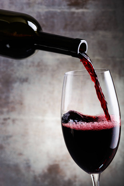Verser du vin rouge dans le verre sur un fond en bois. Bouteille. - Photo, image
