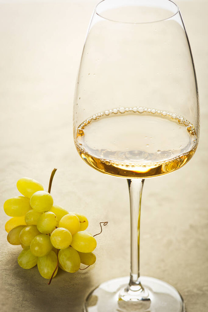 On the table is a glass of white wine and a bunch of grapes. - Photo, Image