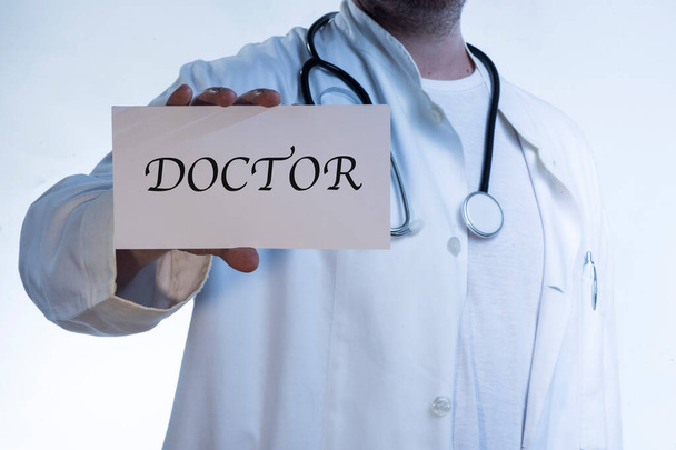 Lekarz w białej koszuli, noszący stetoskop na szyi, trzymający napis "DOKTOR" - Zdjęcie, obraz
