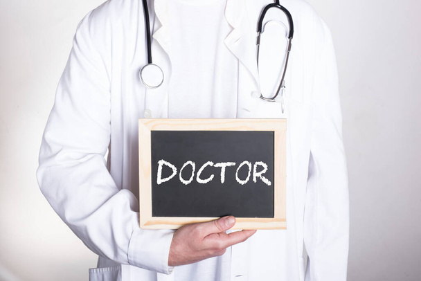 doctor en camisa blanca usando un estetoscopio alrededor de su cuello sosteniendo una pequeña pizarra que dice DOCTOR - Foto, Imagen