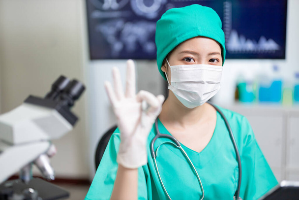asian female doctor who is wearing surgical gown looks to you with ok gesture - Photo, Image