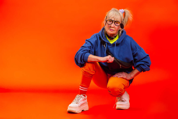 Senior woman in ultra trendy attire isolated on bright orange background - Фото, изображение