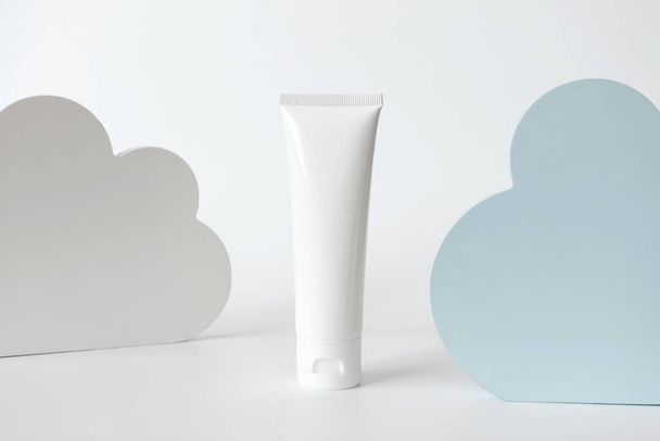 Delicate rejuvenating night cream and blue and white clouds decor. Concept sensitive skincare moisture. Universal mockup white cosmetic plastic tube for cream, lotion, facial cleanser - Photo, Image