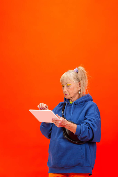 Senior woman in ultra trendy attire isolated on bright orange background - Фото, зображення