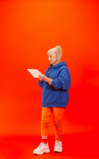 Senior woman in ultra trendy attire isolated on bright orange background - Foto, Imagen