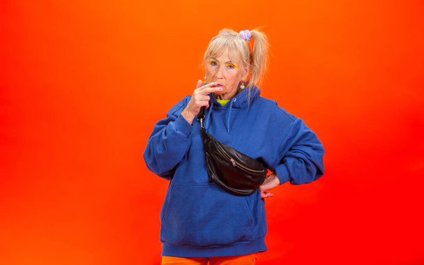 Senior woman in ultra trendy attire isolated on bright orange background - Photo, image