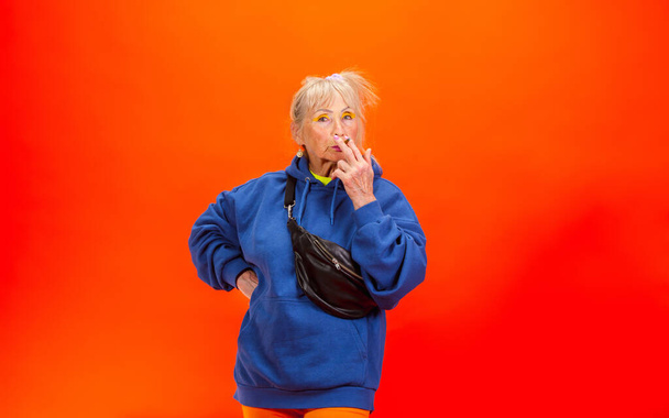 Senior woman in ultra trendy attire isolated on bright orange background - Foto, Bild