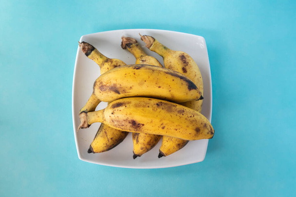 Bunch of ripe bananas on white plate on blue background. Top view. Close up stock photo. - Fotoğraf, Görsel