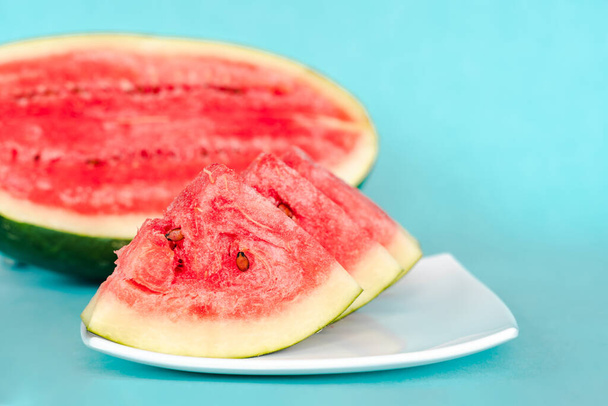 Wassermelonenscheiben auf einem Teller auf blauem Hintergrund. Saftiges, frisches, leckeres Sommerdessert. Archivbild - Foto, Bild