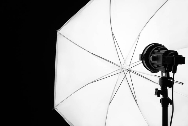 Professzionális stúdió reflektorfény fehér esernyő szerelt stand fekete háttér, closeup - Fotó, kép