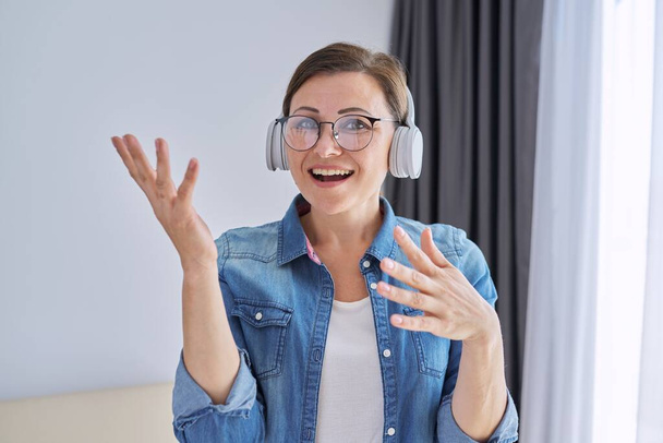 Mature positive talking middle aged woman in headphones looking at camera - Photo, image