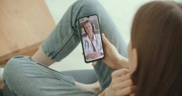 Asistente médica femenina usa bata blanca, auriculares video llamadas paciente distante en el teléfono inteligente. Doctor hablando con el cliente utilizando la aplicación de teléfono de chat virtual. Telemedicina, servicios de salud a distancia  - Imágenes, Vídeo