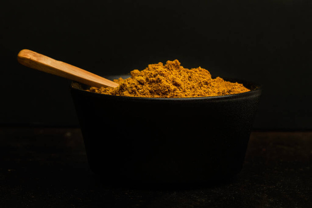 Curry-Pulver in einer schwarzen Schüssel auf dunklem Hintergrund - Foto, Bild