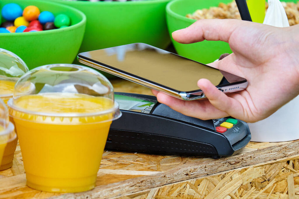 Een persoon betaalt voor voedsel met een contactloos systeem NFC aan de telefoon. - Foto, afbeelding