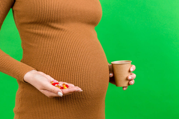 Közelkép terhes nő kezében egy pohár vizet az egyik kezében, és egy halom tablettát a másik kezében színes háttérrel fénymásolás. Gyógyszer szedése a terhesség alatt. - Fotó, kép