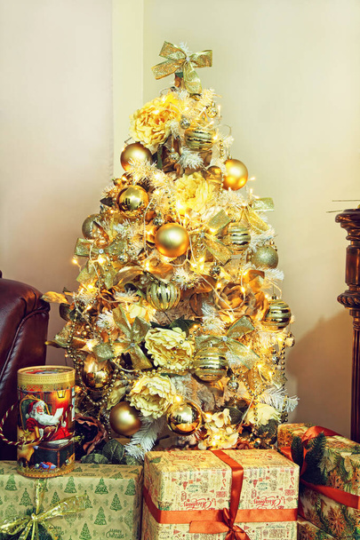 Christmas and new year. Christmas fir-tree with golden christmas decorations and gift boxes in home interior. - Foto, imagen