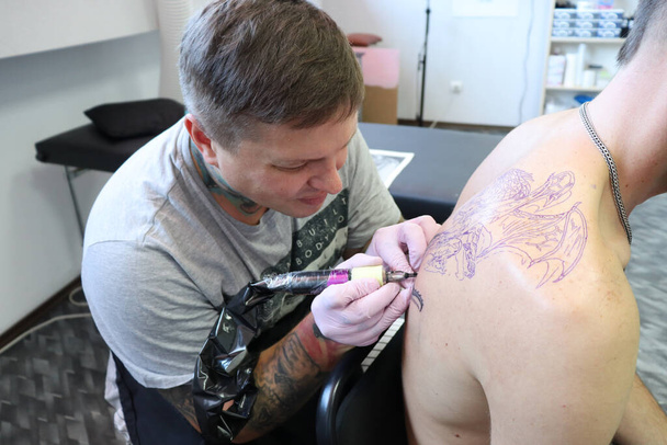 Tattoo master nel salone applica vernice sulla pelle dell'uomo - Foto, immagini