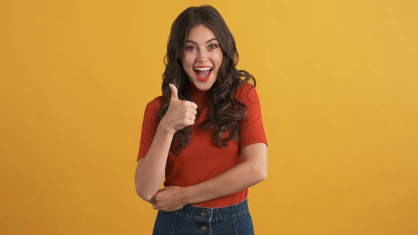 Aantrekkelijk lachend brunette meisje vrolijk tonen duim omhoog op camera over kleurrijke achtergrond. Net als uitdrukking - Foto, afbeelding