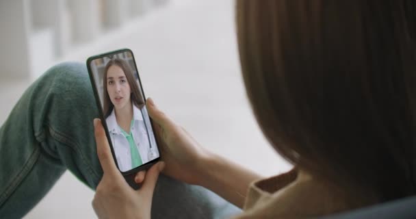 女性は、オンラインビデオチャットを使用して、医師との可能な症状をチェックします。若い女の子は、ビデオ会議医療アプリを介して彼女の医者に話すためにスマートフォンを使用して自宅で病気. - 映像、動画