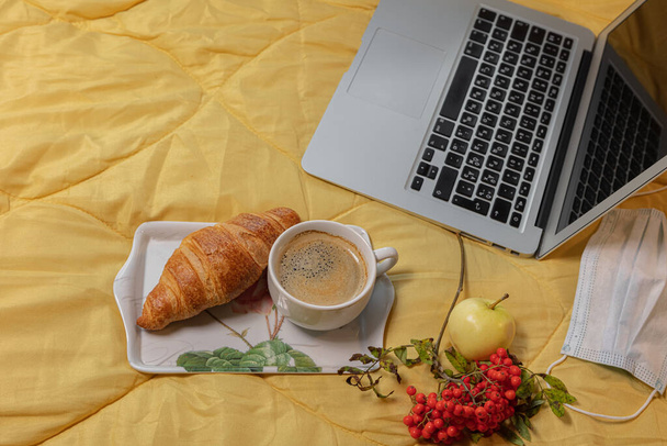  Layout, still life, laptop on a yellow blanket, coffee, bun, medical mask Corontin concept, remote work, training during coronavirus - 写真・画像