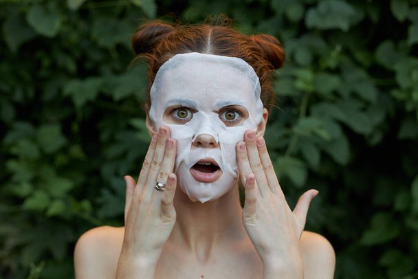 Schöne Frau Anti-Aging-Maske Überrascht, Ihr Gesicht mit Ihren Händen zu berühren nackten Schultern Büsche im Hintergrund - Foto, Bild