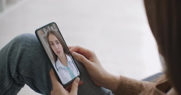 医療アプリを使っている女性はビデオ会議で医師と相談しています。オンラインチャットを使用して家族療法士と話をし、コロナウイルスのパンデミックの間に起こりうる症状をチェックする女性. - 映像、動画