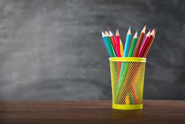 Цветные карандаши в ручке стоят на деревянном столе на фоне черной доски. Копирование пространства. - Фото, изображение